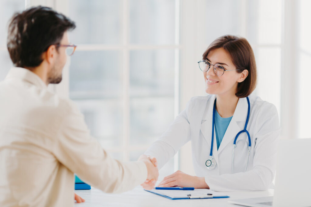 Freundliche Ärztin schüttelt einem Patienten die Hand, symbolisierend die persönliche Gesundheitsberatung und Facharztvermittlung durch die betriebliche Krankenversicherung.